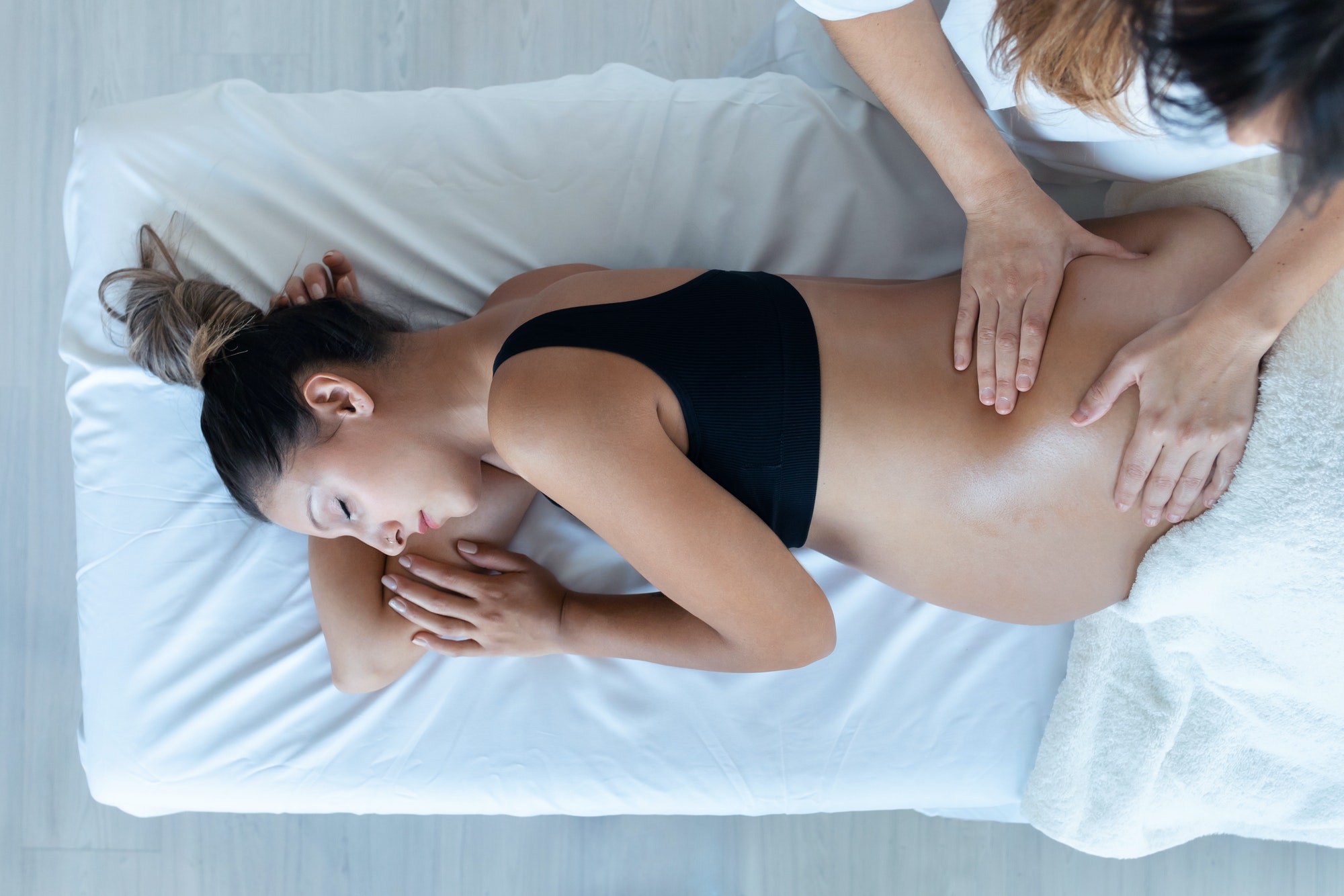 Beautiful young physiotherapist woman massaging tummy on pregnant woman on a stretcher at home.