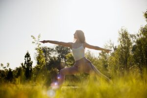 Young woman in yoga clothes is practising yoga in the open air in the nature on the grass on the